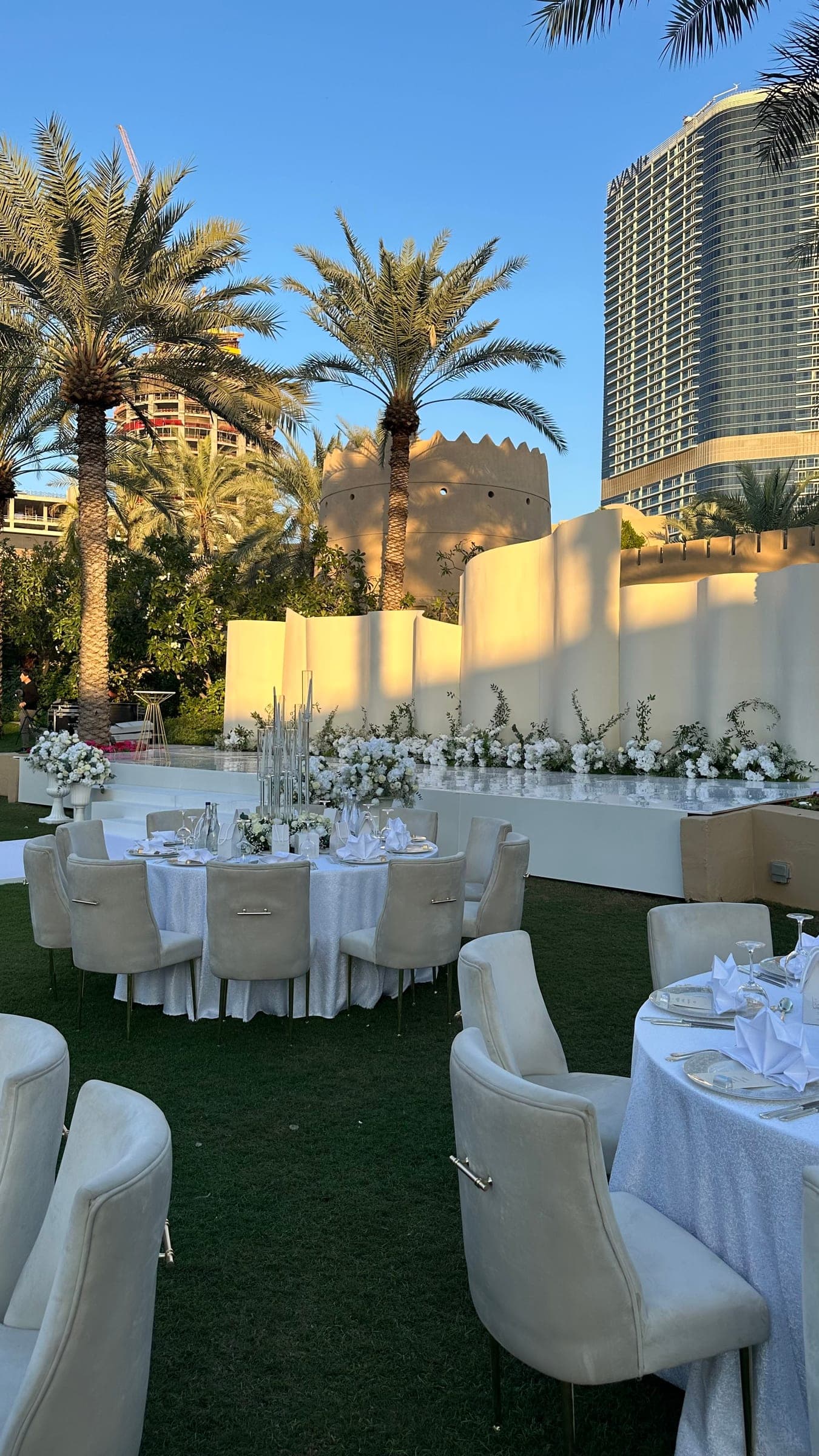 Round tables dressed in white on the lawn, facing a curved ivory stage with white florals