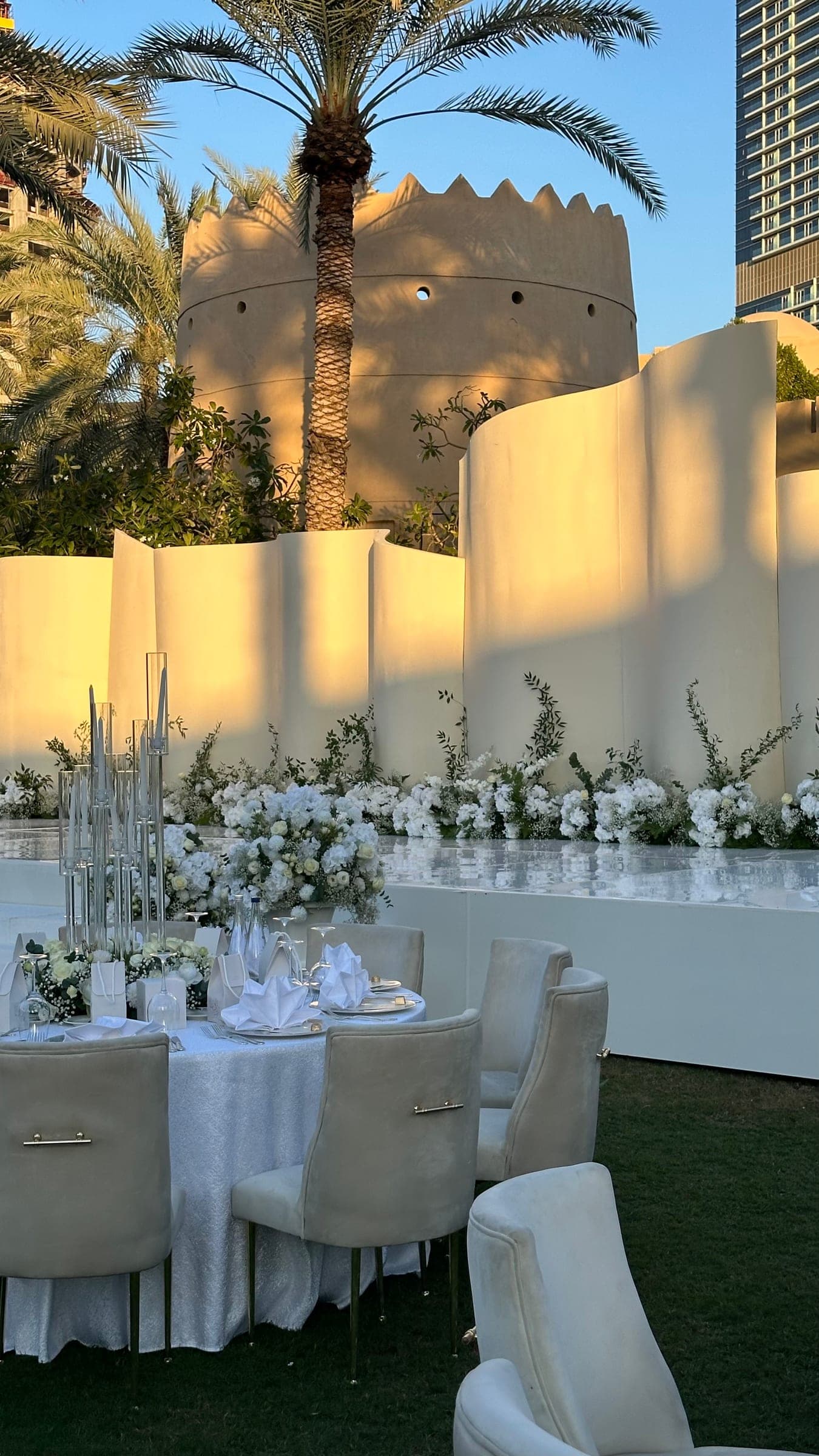 Curved ivory panels in late-afternoon light, with white florals and greenery along the stage and a set table in front