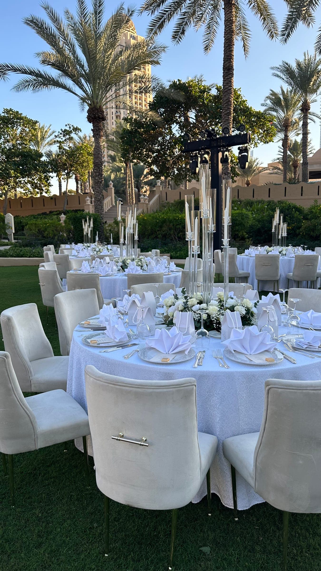 A round table set in white with a tall candelabra and white florals, other tables and palms behind
