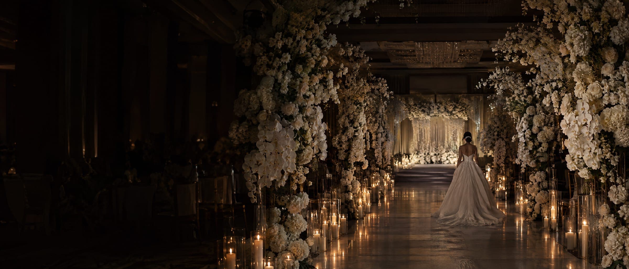 Concept image: a candlelit wedding aisle between tall ivory floral arches, a bride walking toward the stage