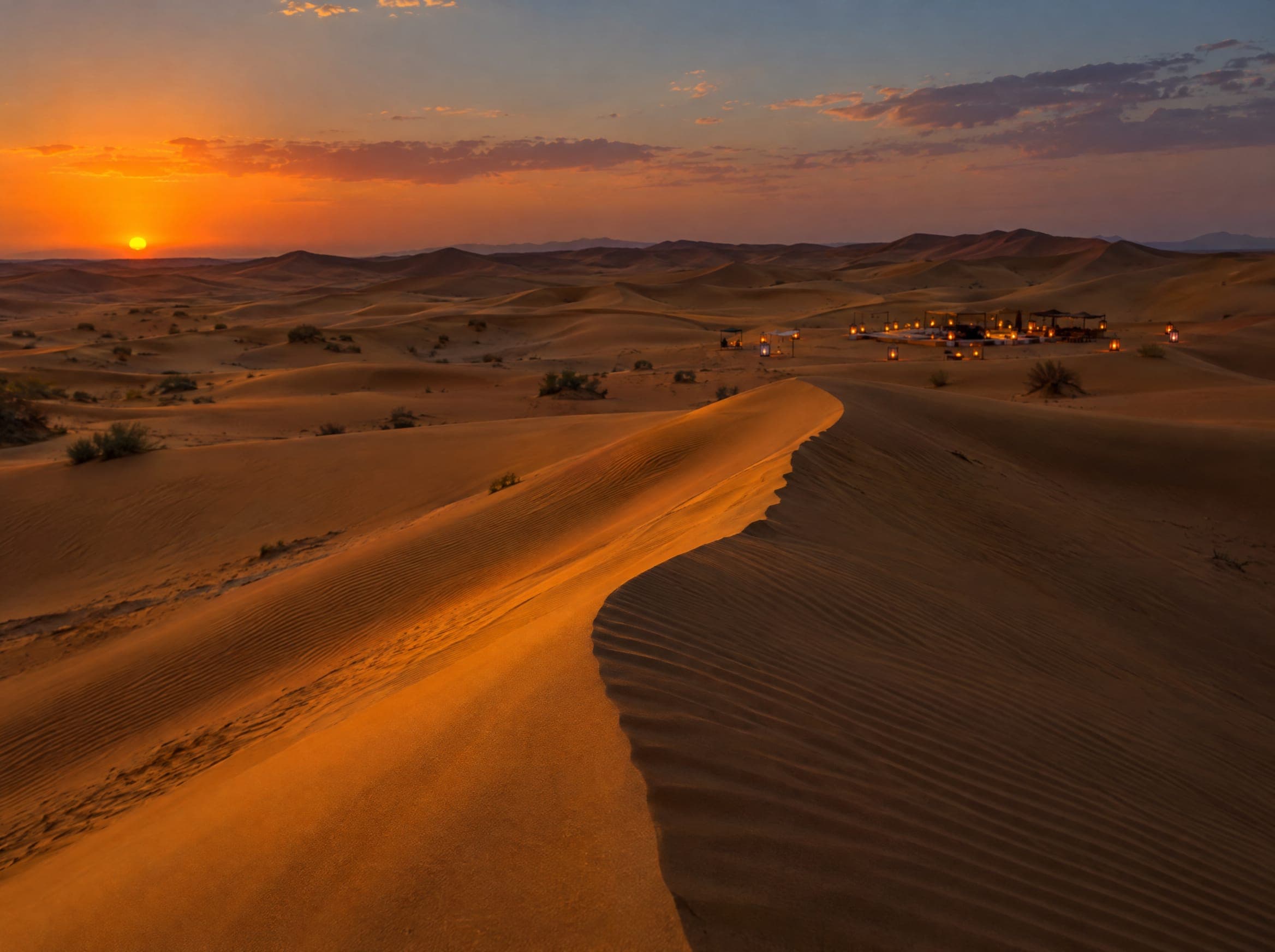 Sand dunes at sunset with distant lanterns