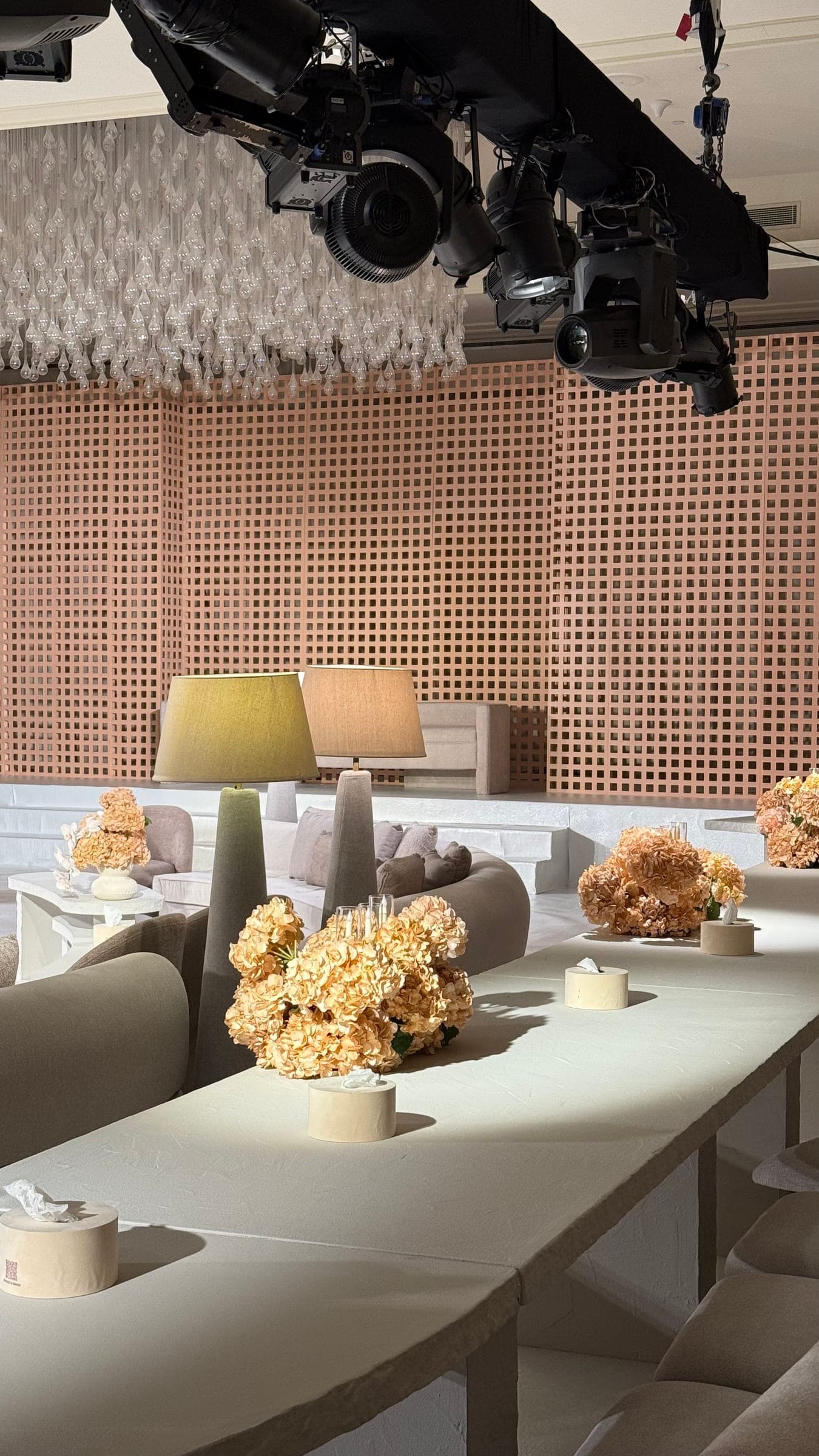 Apricot hydrangeas and candles on a long table, with lamps and lounge seating behind and lights on a truss above