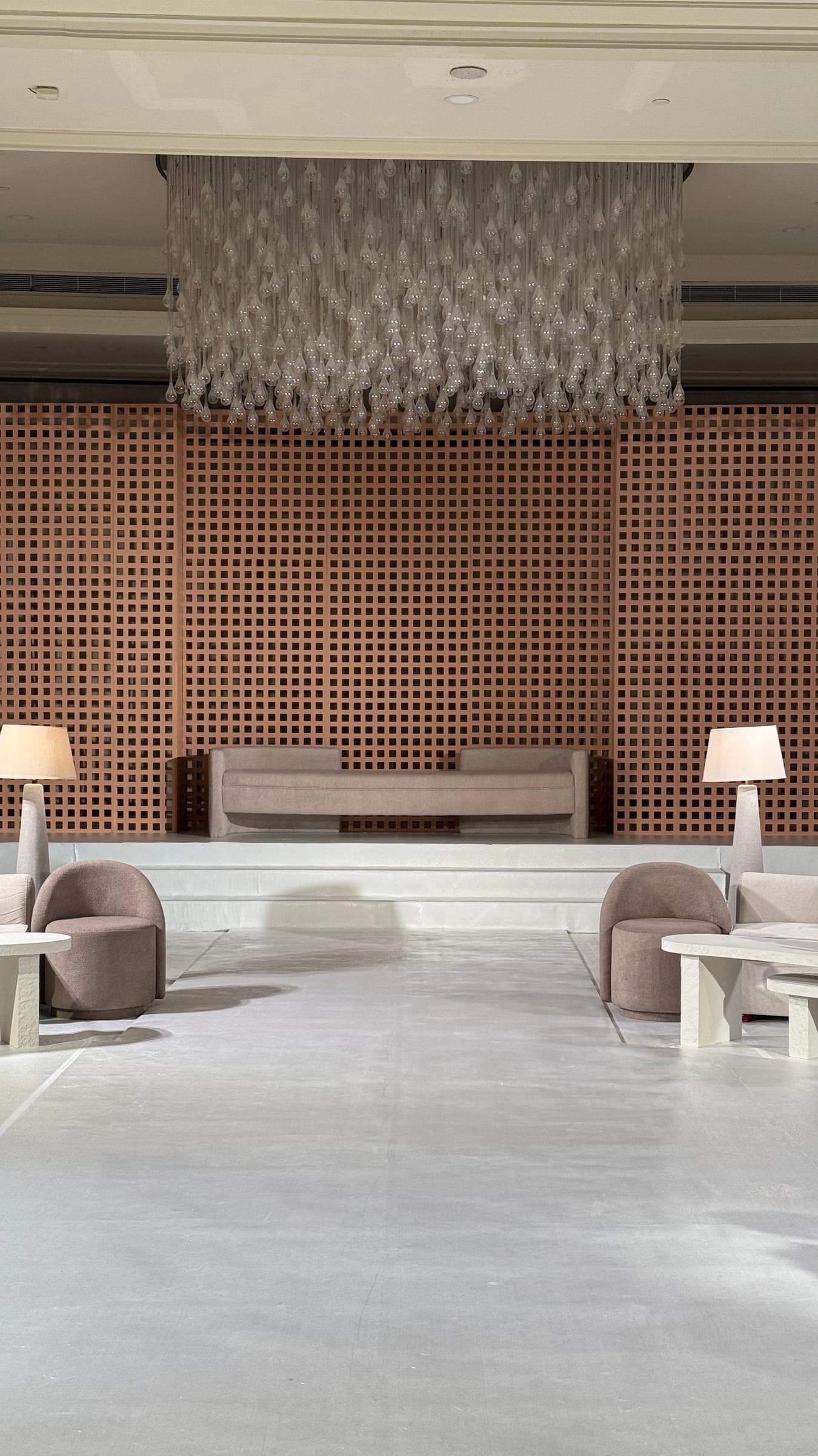 A raised seating platform with lamps before a terracotta lattice wall, beneath a suspended crystal installation