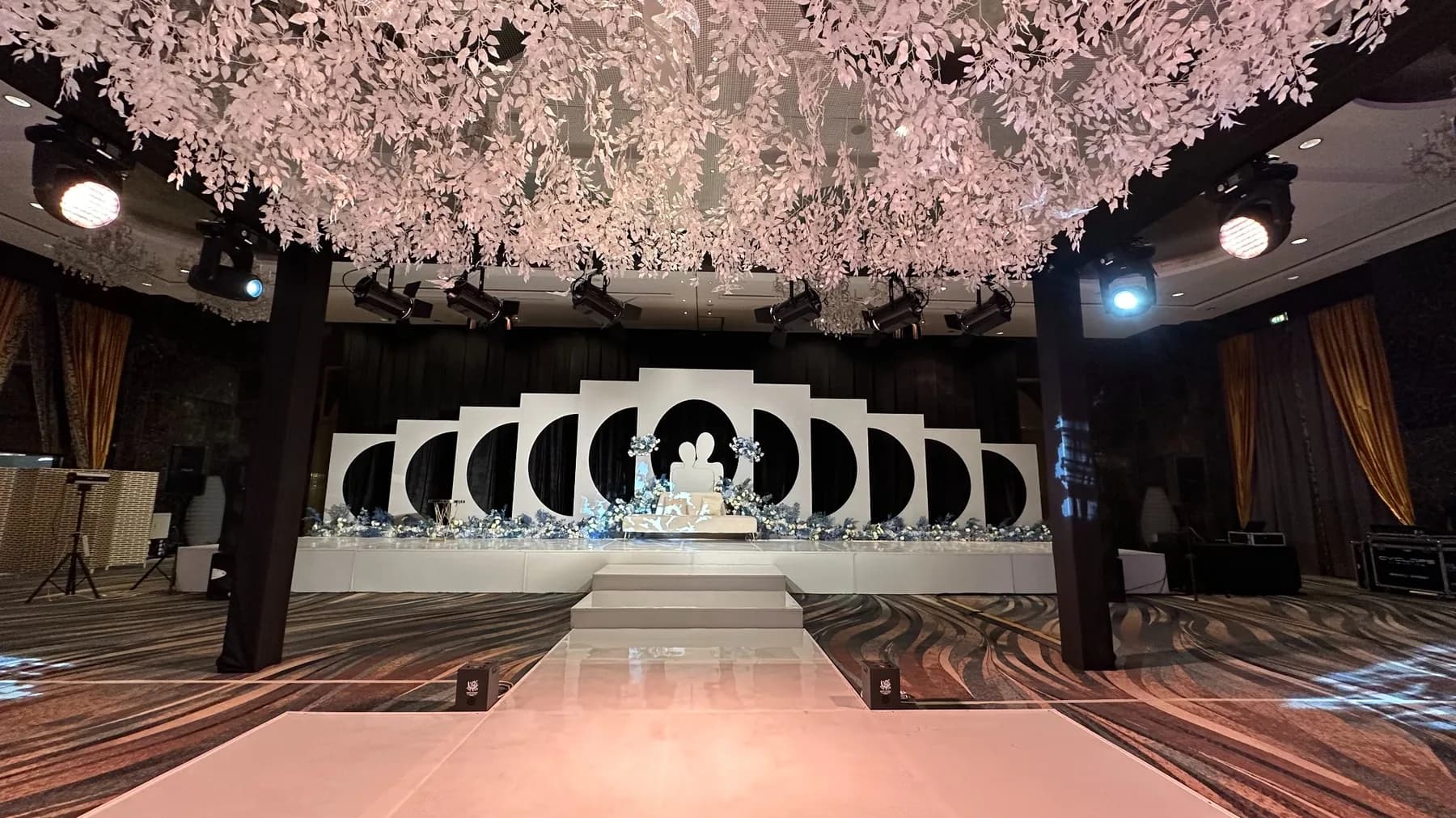 Raffles Dubai ballroom with a glossy pale aisle, black overhead frame, white hanging foliage and a black-and-white geometric kosha