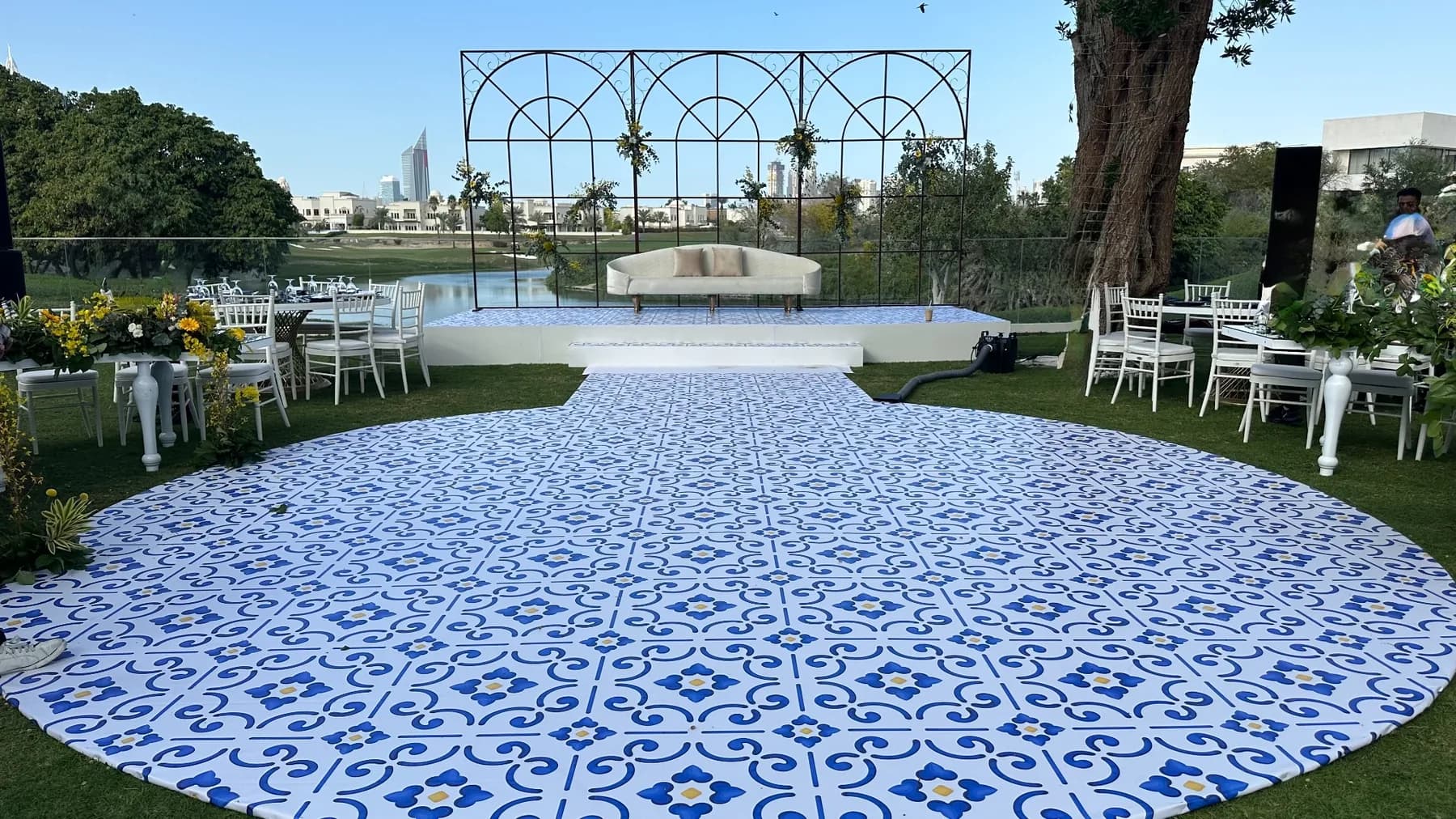 An outdoor blue-and-white patterned dance floor at Address Montgomerie, with white seating and yellow floral tables around it